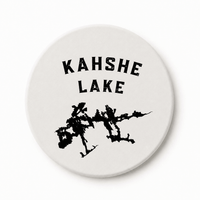 Round white ceramic coaster with Kahshe Lake lettering and black lake silhouette