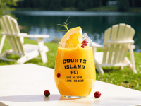 Personalized Courts Island PEI acrylic wine glass with an orange drink and fruit garnish on a table beside a lake