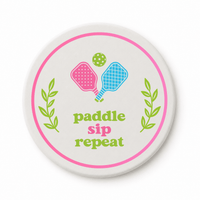 Round ceramic pickleball coaster that says paddle sip repeat with pink and blue paddles